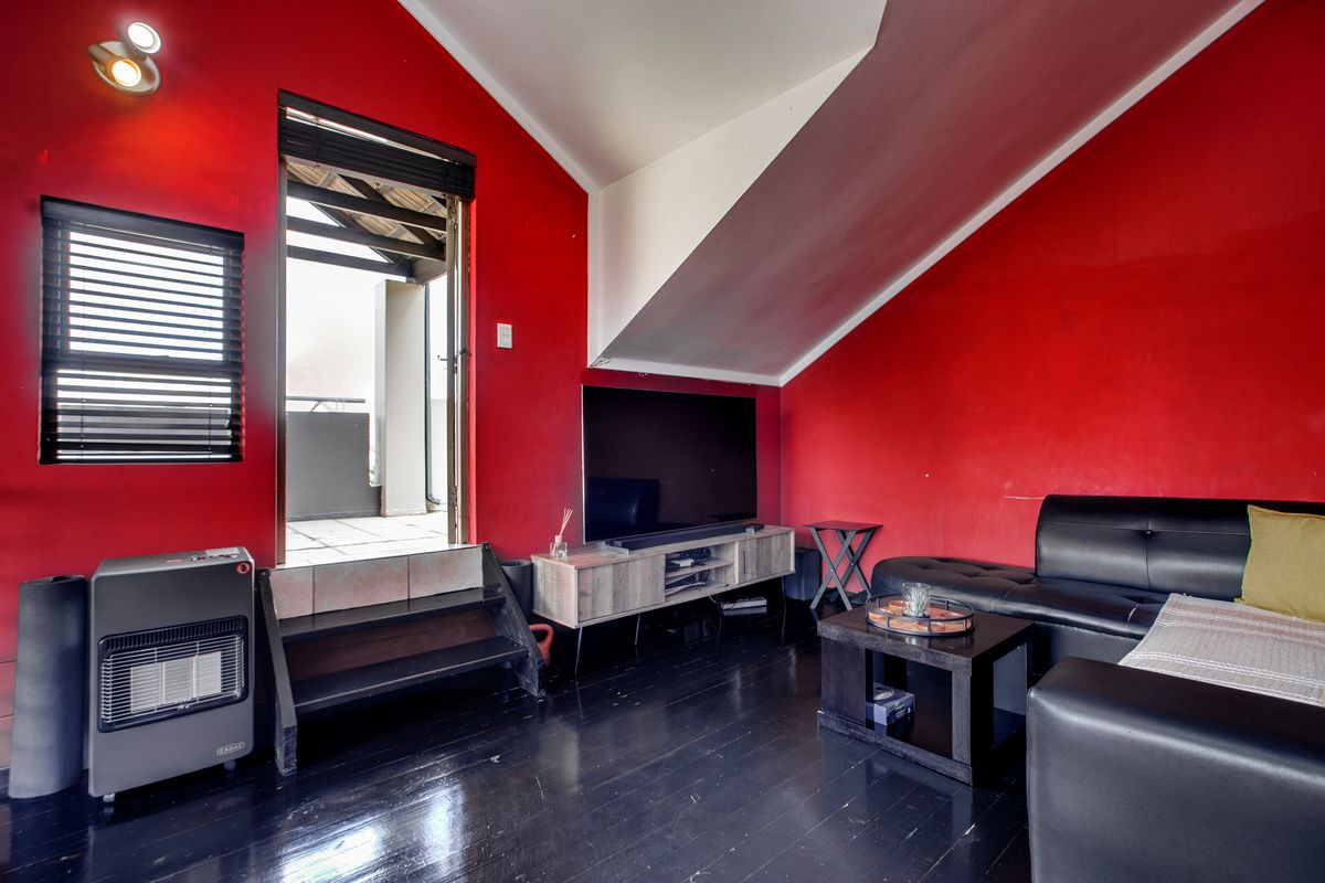 A living room featuring dark timber flooring, vaulted ceilings, and direct access to an outdoor balcony area.