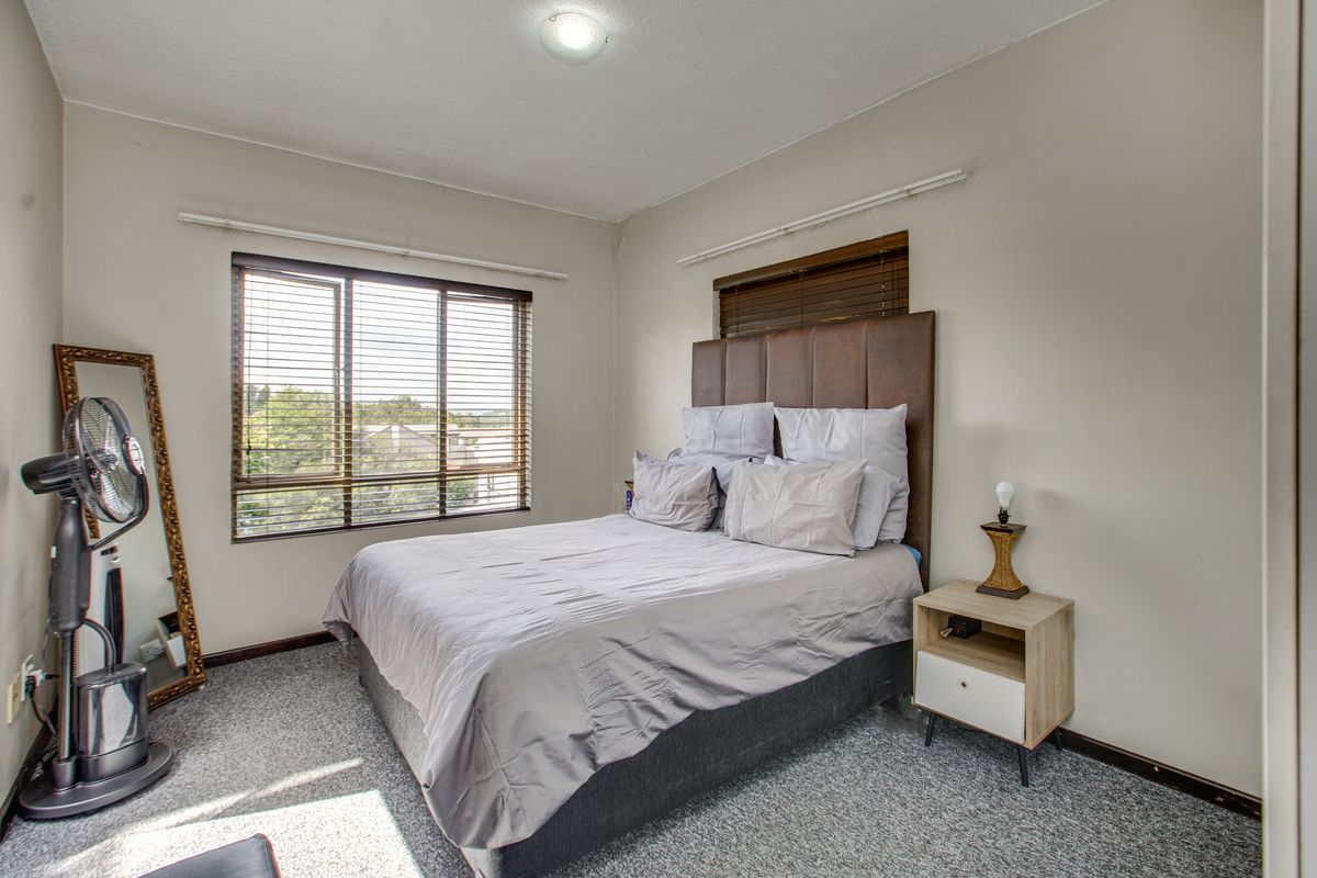 A functional bedroom featuring carpeted flooring, large windows with fitted blinds, and a neutral color palette, offering a comfortable living space.
