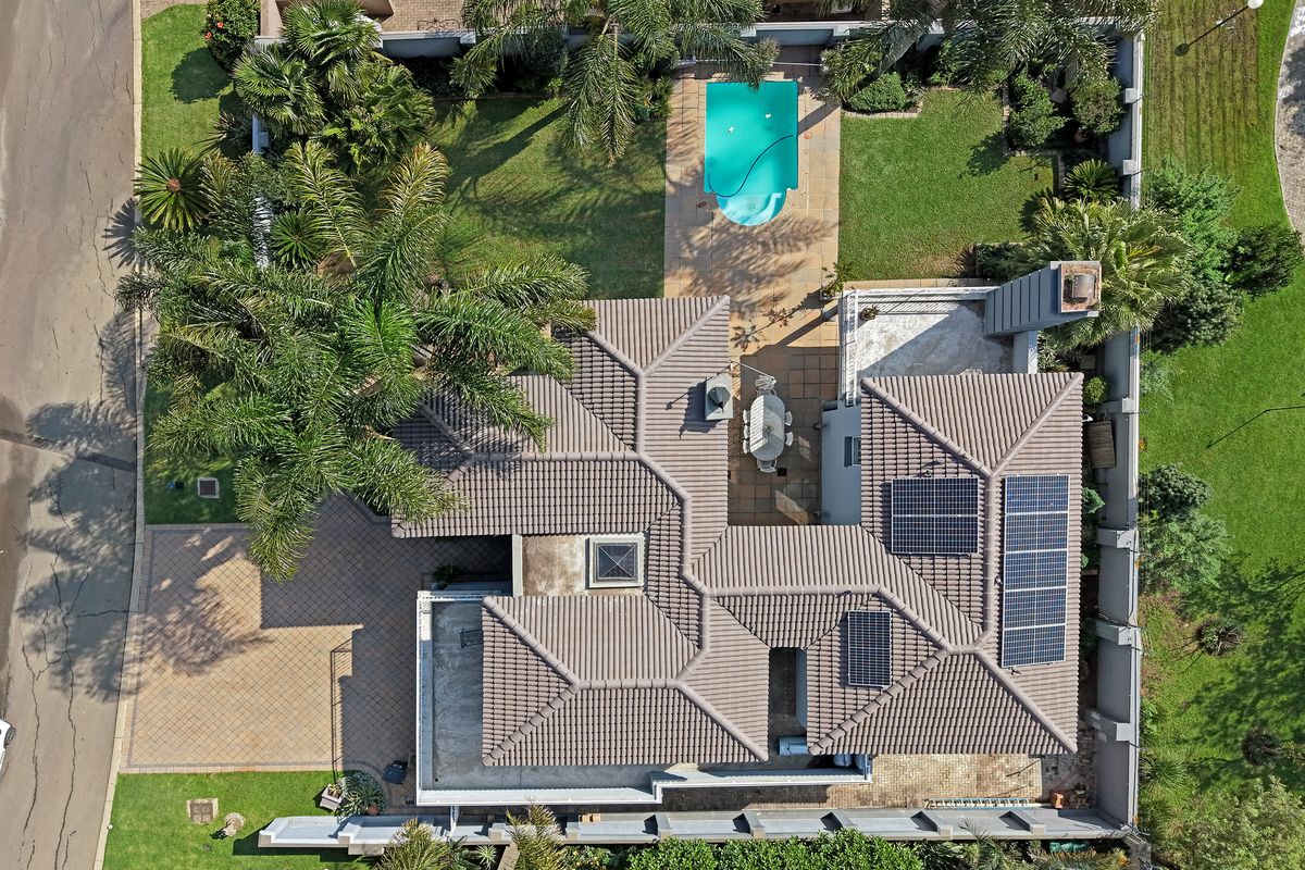 Aerial view of the property featuring a tiled roof, solar panels, a swimming pool, paved driveway, and landscaped garden areas.