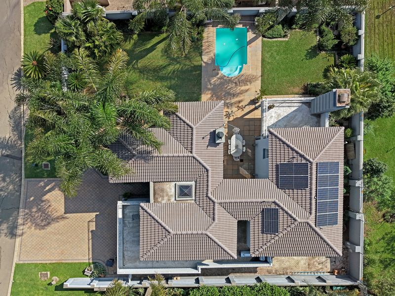Aerial view of the property featuring a tiled roof, solar panels, a swimming pool, paved driveway, and landscaped garden areas.