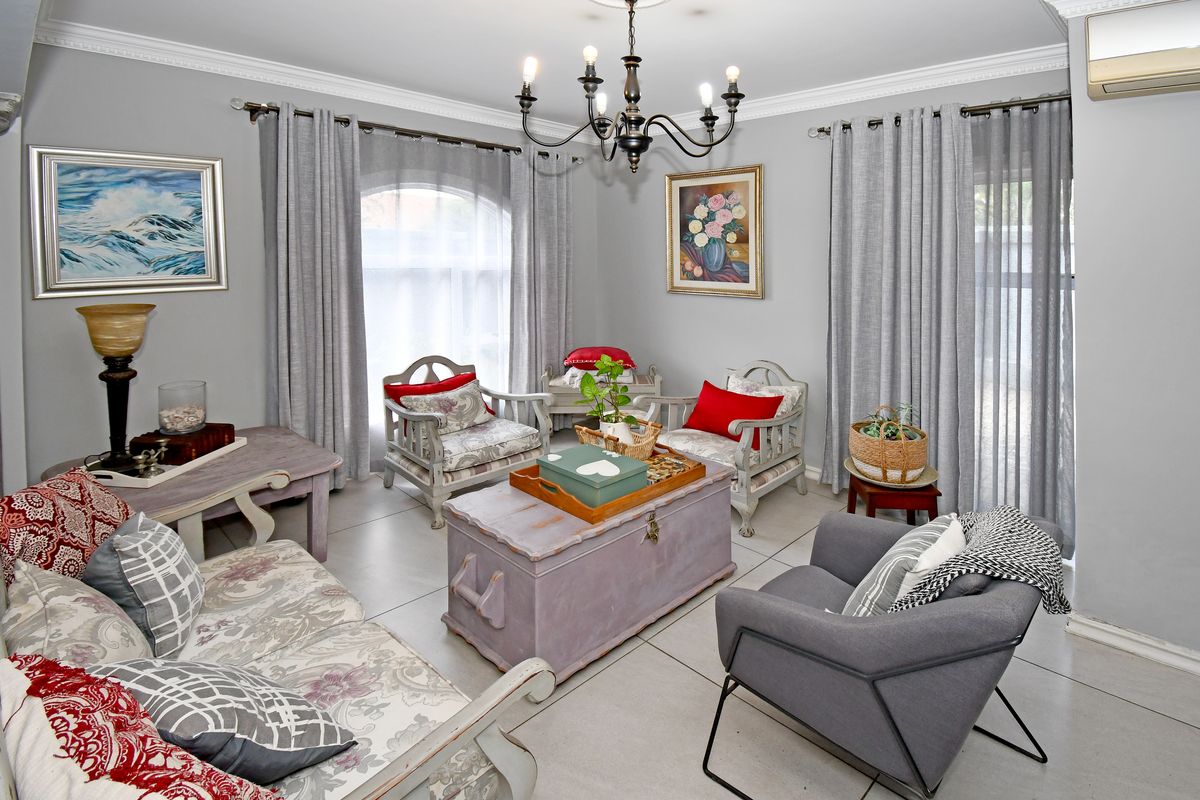 A well-maintained living room featuring tiled flooring, crown molding, a classic chandelier, and large windows with neutral curtains.