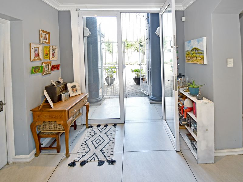 A bright entry foyer featuring tiled flooring, crown molding, and glass double doors opening onto a paved patio area with decorative columns.