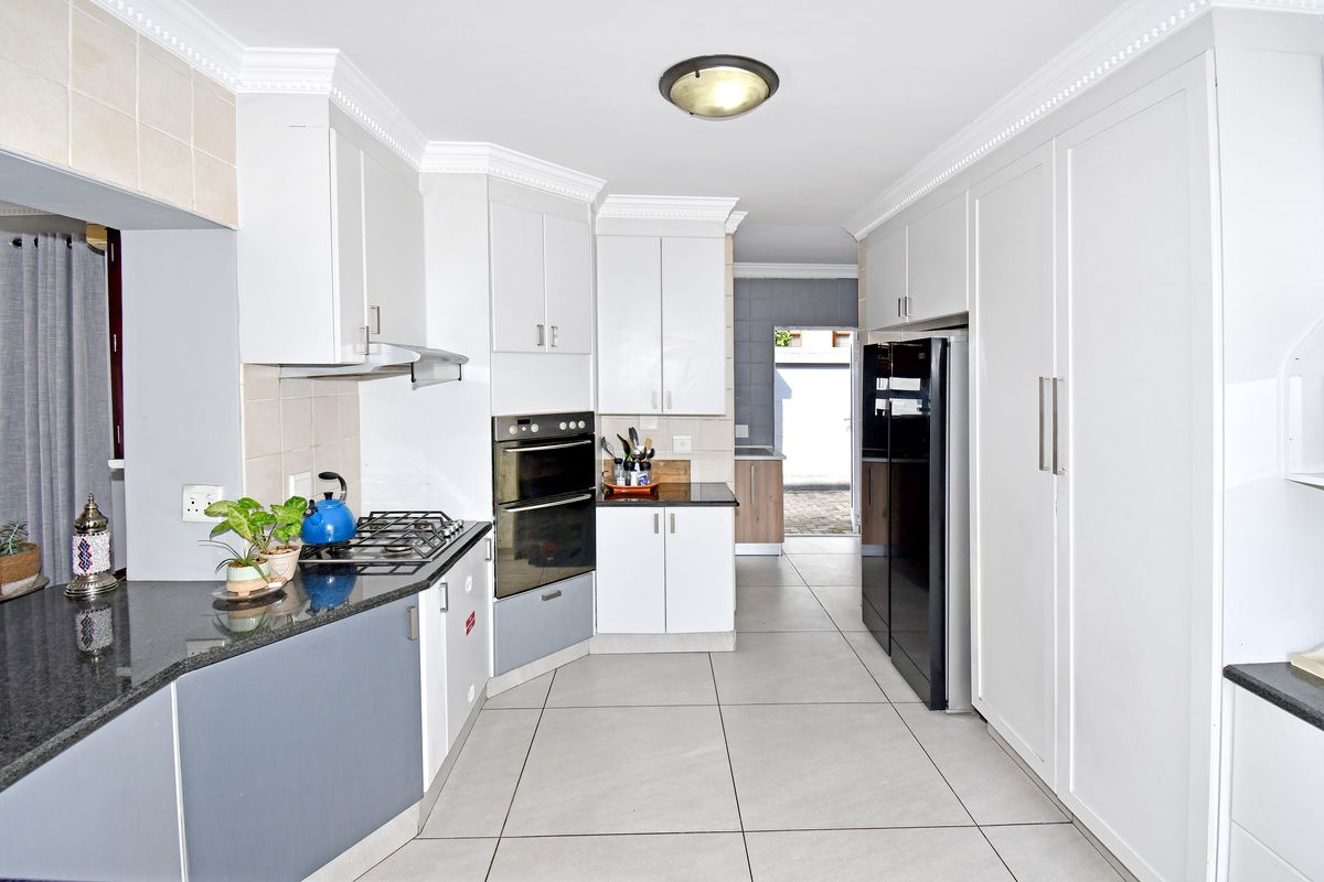 A modern kitchen featuring white cabinetry, granite countertops, a built-in oven, gas hob, extractor fan, and large format floor tiles.