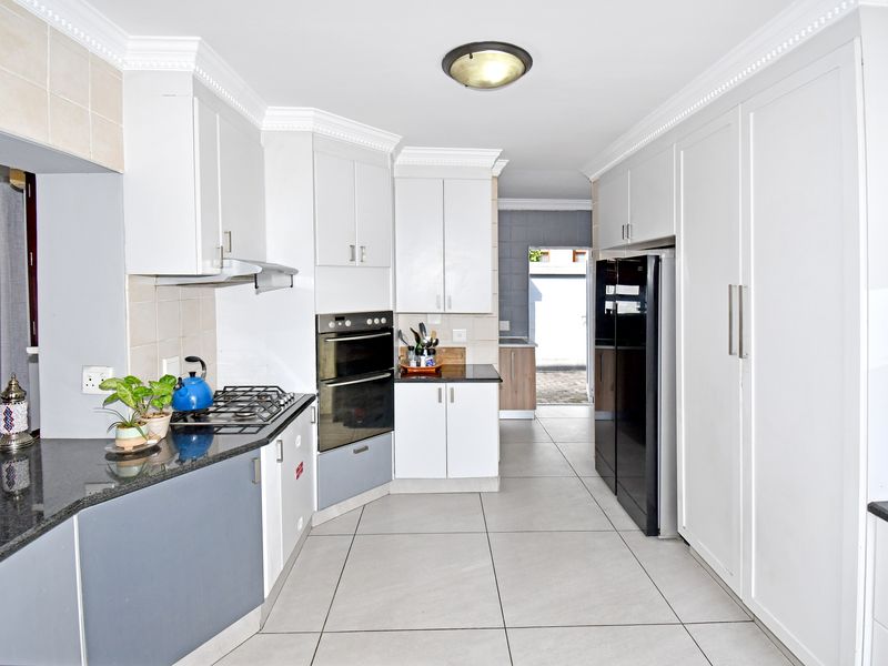 A modern kitchen featuring white cabinetry, granite countertops, a built-in oven, gas hob, extractor fan, and large format floor tiles.