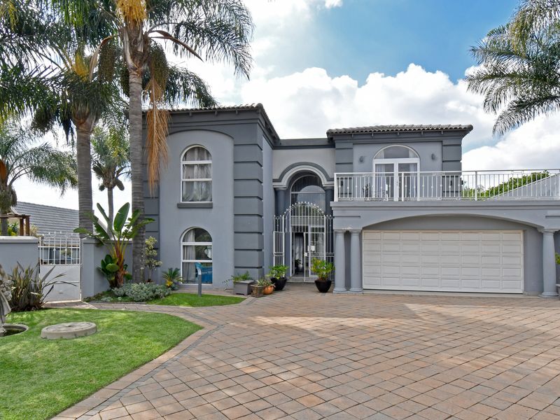 A well-maintained double-story residence featuring a paved driveway, integrated double garage, arched windows, and a balcony with decorative metal railings.