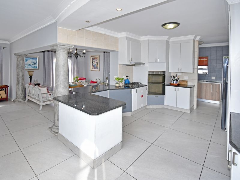 Open-plan kitchen featuring granite countertops, built-in double oven, gas hob, and extractor fan, seamlessly flowing into the adjacent living area with decorative columns.