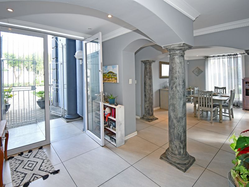 Open-plan living and dining area featuring decorative columns, tiled flooring, and large glass doors providing seamless access to the outdoor patio.