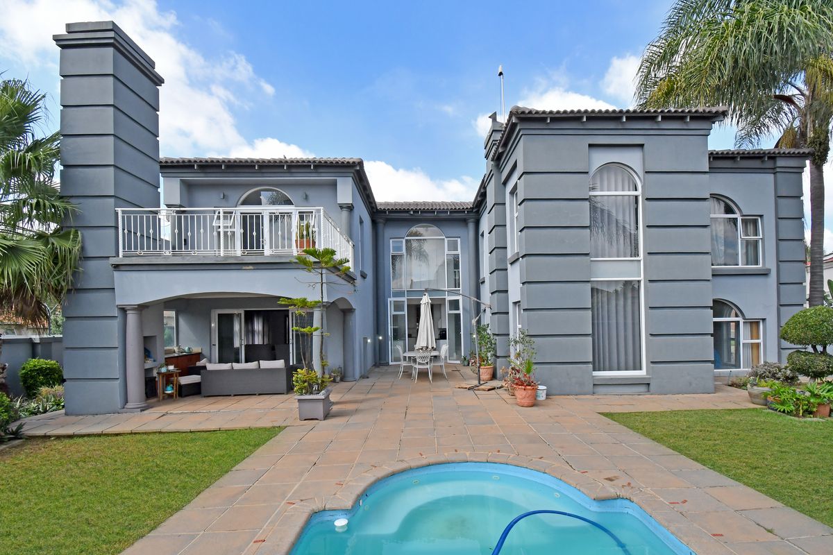 Rear view of a multi-story residence featuring a paved patio, swimming pool, balcony, and large arched windows with a grey exterior finish.