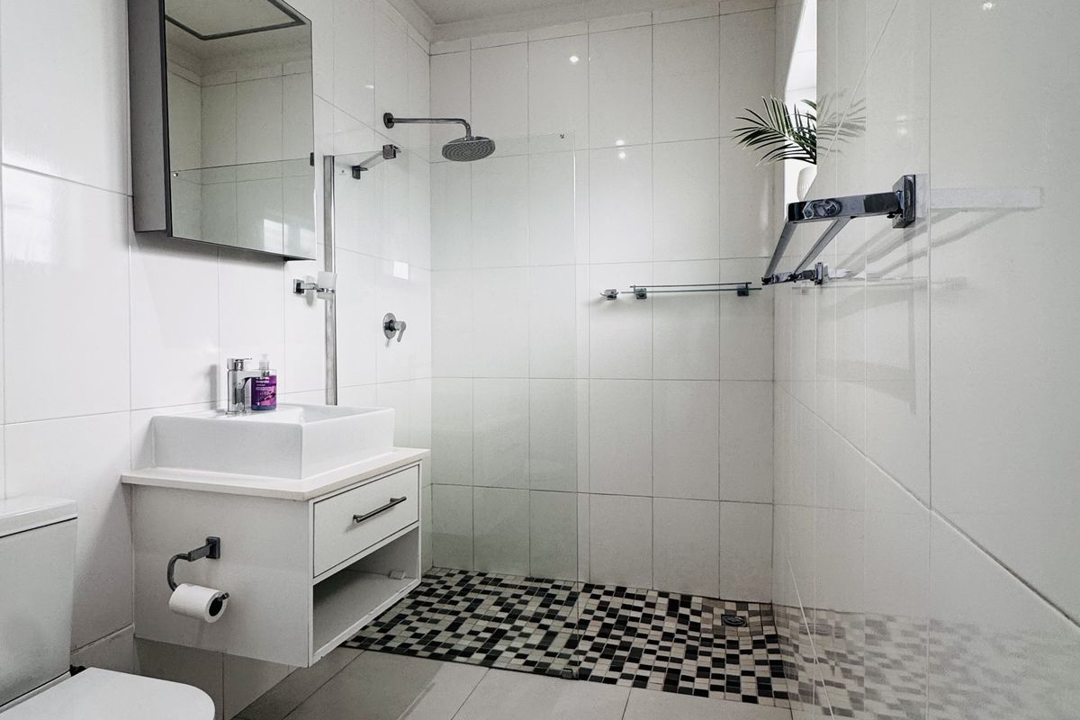 Modern bathroom featuring a walk-in shower with mosaic tile flooring, a wall-mounted vanity with a vessel sink, and a sleek glass shower screen.