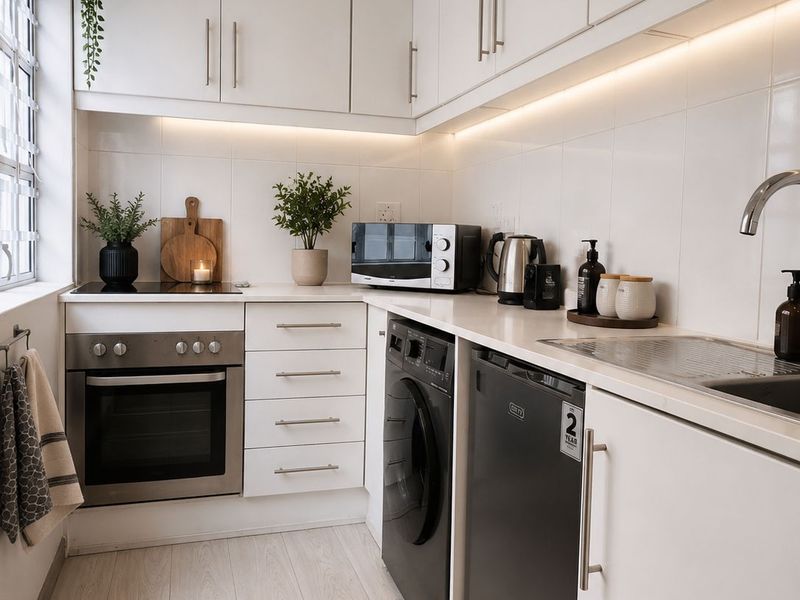 A modern, well-maintained kitchen featuring white cabinetry, integrated appliances, under-cabinet lighting, and a clean tiled backsplash.