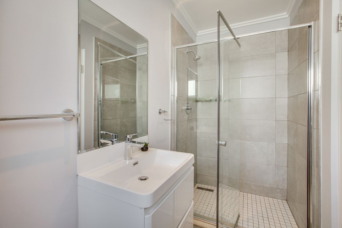 Modern bathroom featuring a sleek vanity with basin, large wall mirror, and a walk-in shower with glass enclosure and neutral wall tiling.