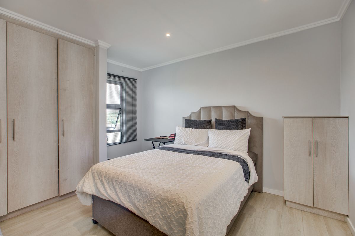 A well-maintained bedroom featuring light wood-look flooring, built-in cabinetry, and a window with fitted blinds.