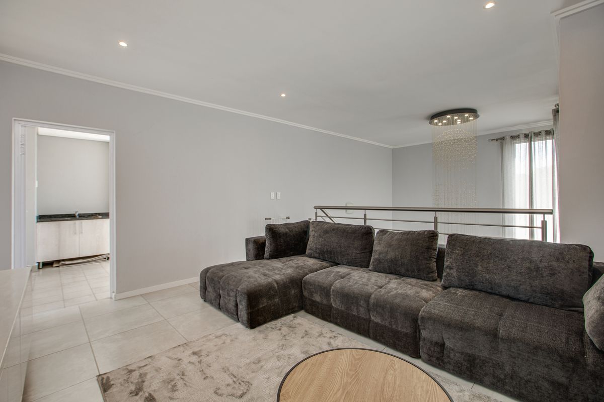 Spacious living area featuring tiled flooring, recessed downlighting, and a metal balustrade overlooking the lower level, with an adjacent room visible.