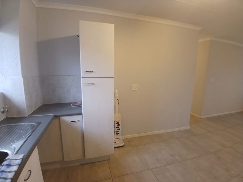 A functional kitchen area featuring built-in white cabinetry, a stainless steel sink, and neutral tiled flooring, offering a clean and simple layout.