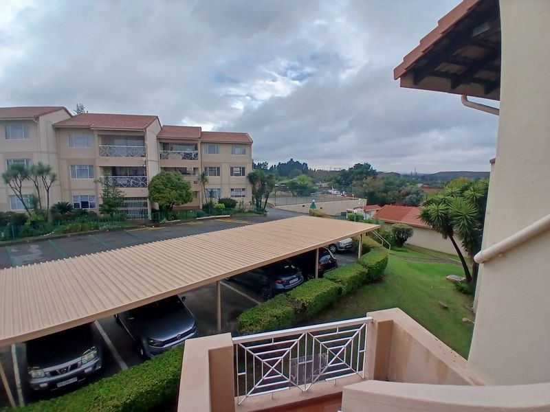 Elevated view overlooking the apartment complex grounds, featuring covered parking bays, landscaped garden areas, and surrounding residential buildings.