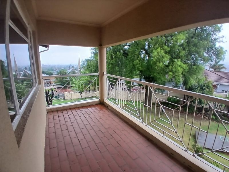 A covered balcony featuring tiled flooring and a decorative metal balustrade, offering an elevated view of the surrounding neighborhood and garden.