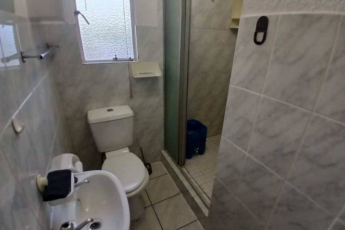 A compact bathroom featuring a pedestal basin, toilet, and a separate shower enclosure with tiled walls and flooring.