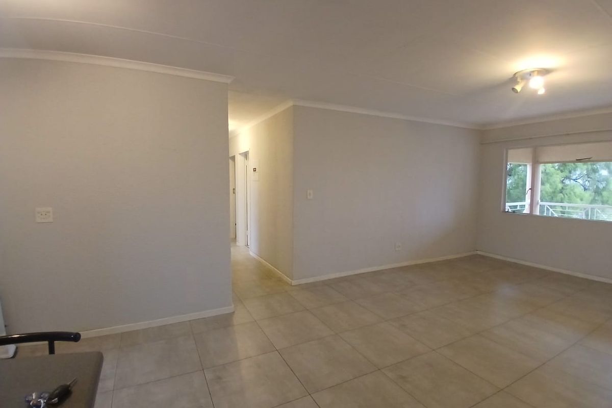 A spacious, empty living area featuring neutral tiled flooring, clean walls, and natural light from a large window.