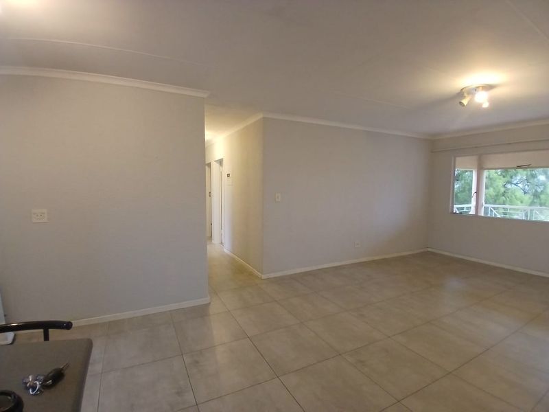 A spacious, empty living area featuring neutral tiled flooring, clean walls, and natural light from a large window.