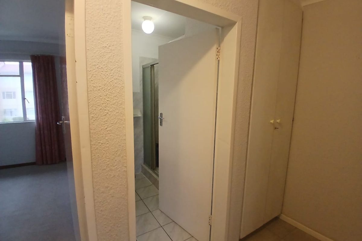 A bedroom featuring built-in cupboards and an en-suite bathroom with a shower enclosure, presented in a clean, vacant state.