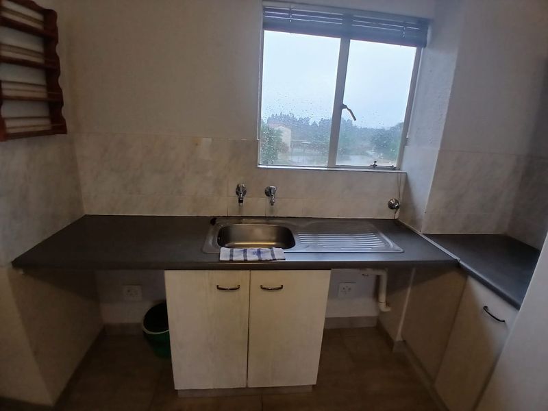 A functional laundry area featuring a stainless steel sink, laminate countertops, and built-in cabinetry with tiled splashbacks.