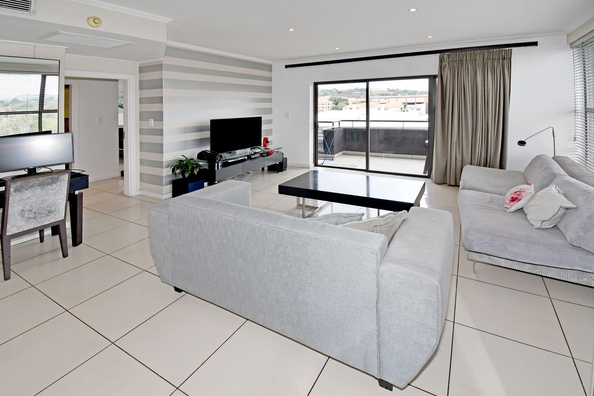 Spacious open-plan living area featuring large format floor tiles, recessed downlighting, and sliding glass doors leading to a private balcony.