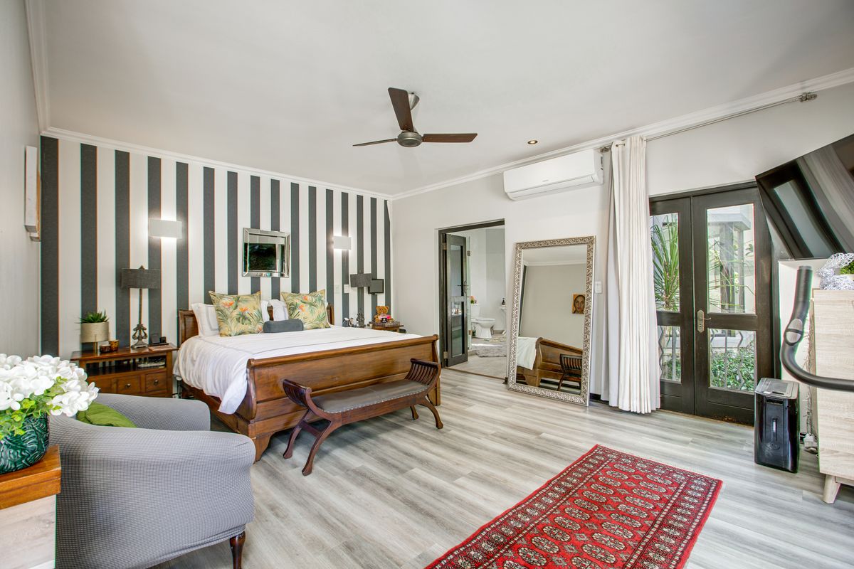 Spacious bedroom featuring wood-look flooring, a ceiling fan, wall-mounted air conditioning unit, and direct access to an en-suite bathroom and outdoor area.