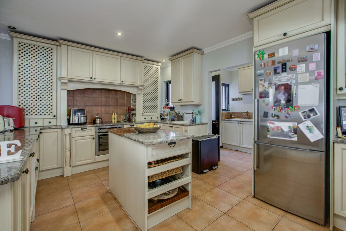 A traditional kitchen featuring cream cabinetry, granite countertops, a central island, and a connected scullery area with tiled flooring.