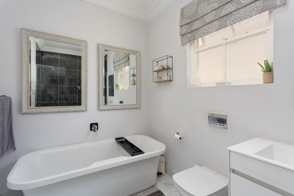 A modern bathroom featuring a freestanding bathtub, wall-mounted toilet with concealed cistern, and a vanity unit with integrated sink.