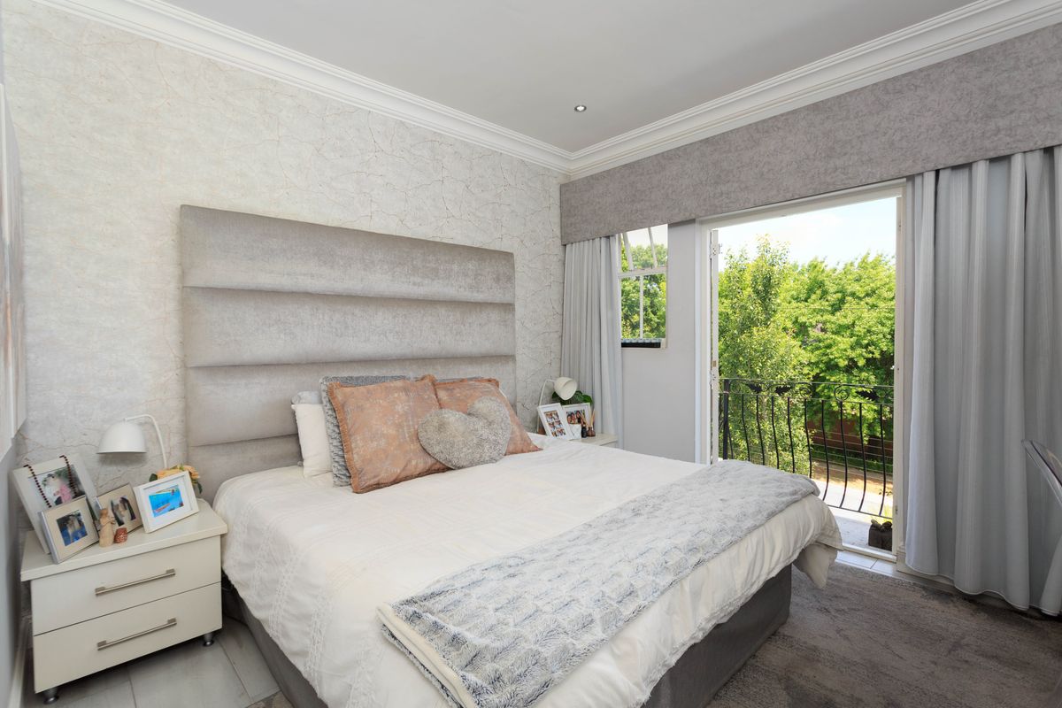 A well-maintained bedroom featuring a built-in headboard, crown molding, and a glass door opening onto a private balcony with garden views.