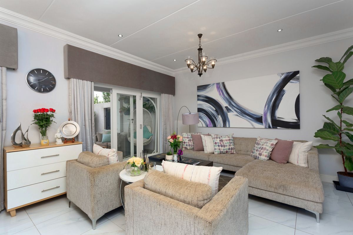 A bright and well-maintained living room featuring tiled flooring, recessed ceiling lighting, decorative crown molding, and sliding glass doors leading to an outdoor area.