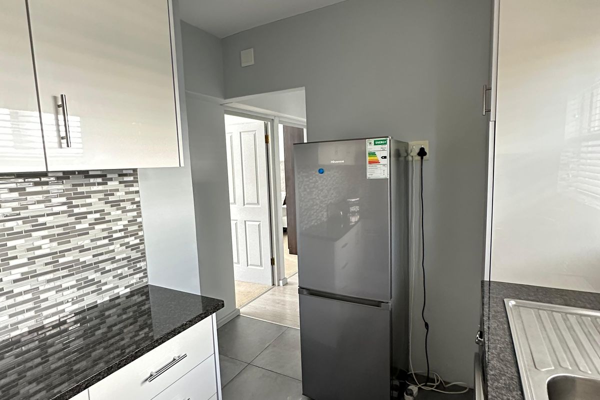 A modern kitchen featuring glossy white cabinetry, granite countertops, a mosaic tile backsplash, and durable tiled flooring.
