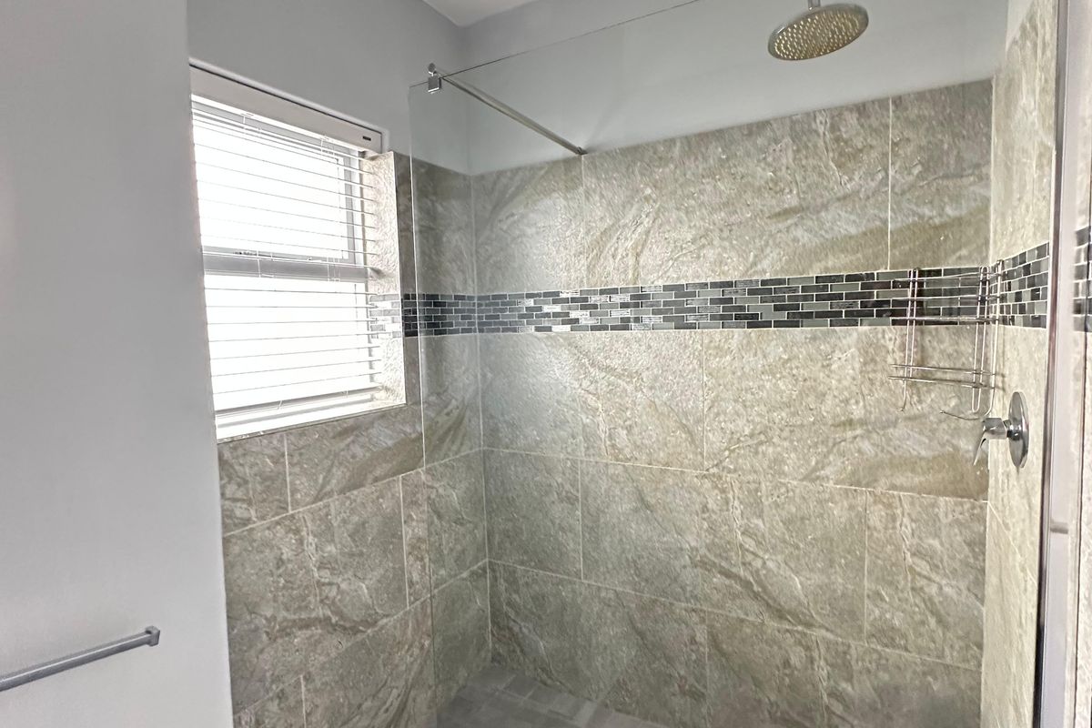 A modern walk-in shower featuring textured stone-look wall tiles, a decorative mosaic accent band, a glass screen, and a rainfall shower head.
