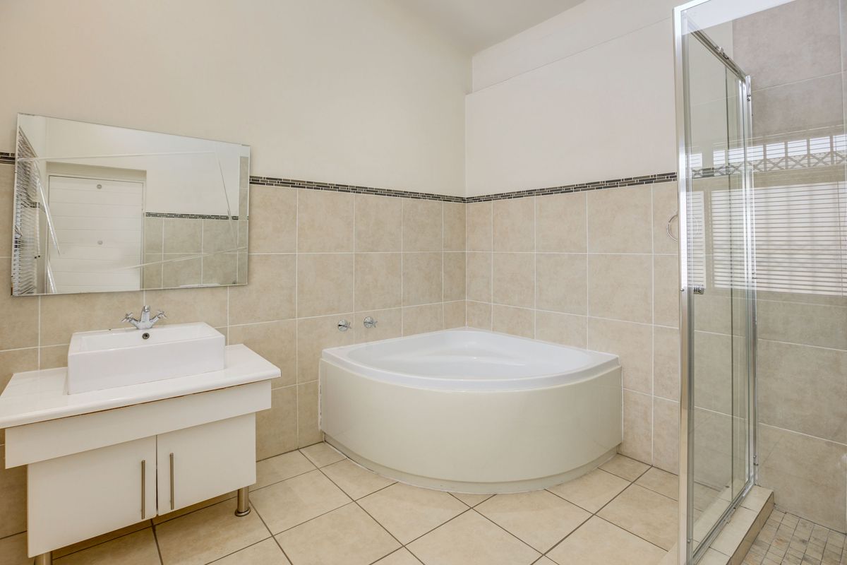 A clean bathroom featuring a corner bathtub, a separate glass-enclosed shower, and a modern vanity with a basin and wall-mounted mirror.
