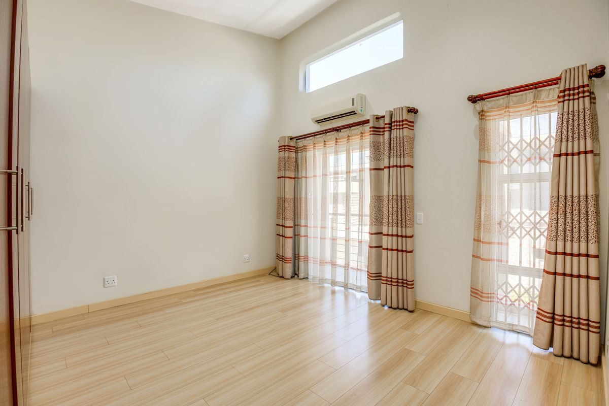 A bright, empty bedroom featuring light wood-look flooring, high ceilings with a clerestory window, built-in cupboards, and a wall-mounted air conditioning unit.