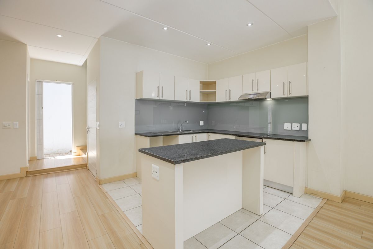 Modern kitchen featuring sleek cabinetry, granite countertops, a breakfast island, and a glass splashback, seamlessly connected to an adjacent living area.
