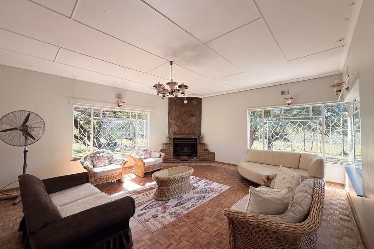 Spacious living room featuring a stone-clad fireplace, large windows with security bars, and traditional parquet flooring.