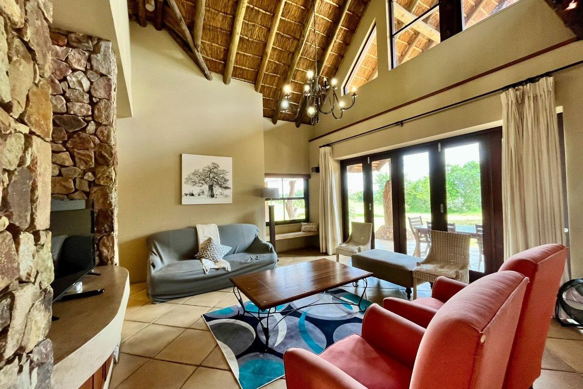Spacious living room featuring a high vaulted thatched ceiling, exposed timber beams, stone-clad fireplace, and large glass doors opening to the outdoor patio.
