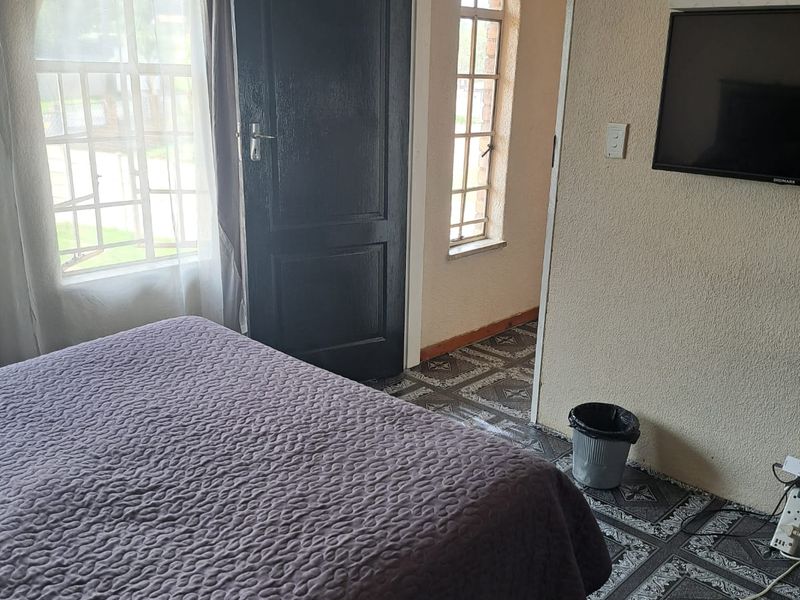 A bedroom featuring arched windows, tiled flooring, and direct access to an adjacent room through a panel door.