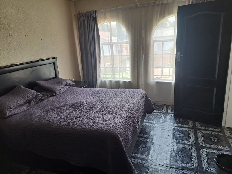 A bedroom featuring arched windows, dark tiled flooring, and a solid core door, requiring cosmetic updates to the wall finishes.