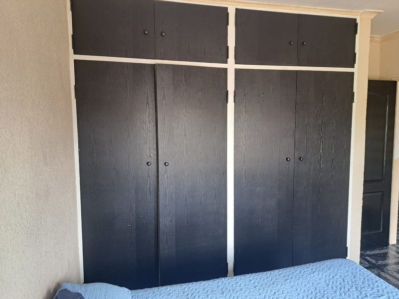 A bedroom featuring dark, built-in floor-to-ceiling cupboards with overhead storage compartments, providing ample integrated storage space.