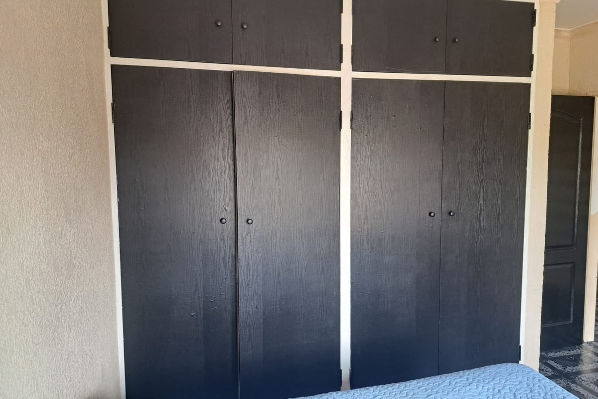 A bedroom featuring dark, built-in floor-to-ceiling cupboards with overhead storage compartments, providing ample integrated storage space.
