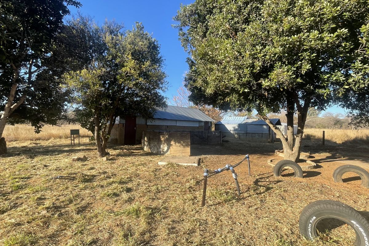 Rear view of a farm building featuring brick construction and a corrugated metal roof, set within a rural landscape with mature trees.