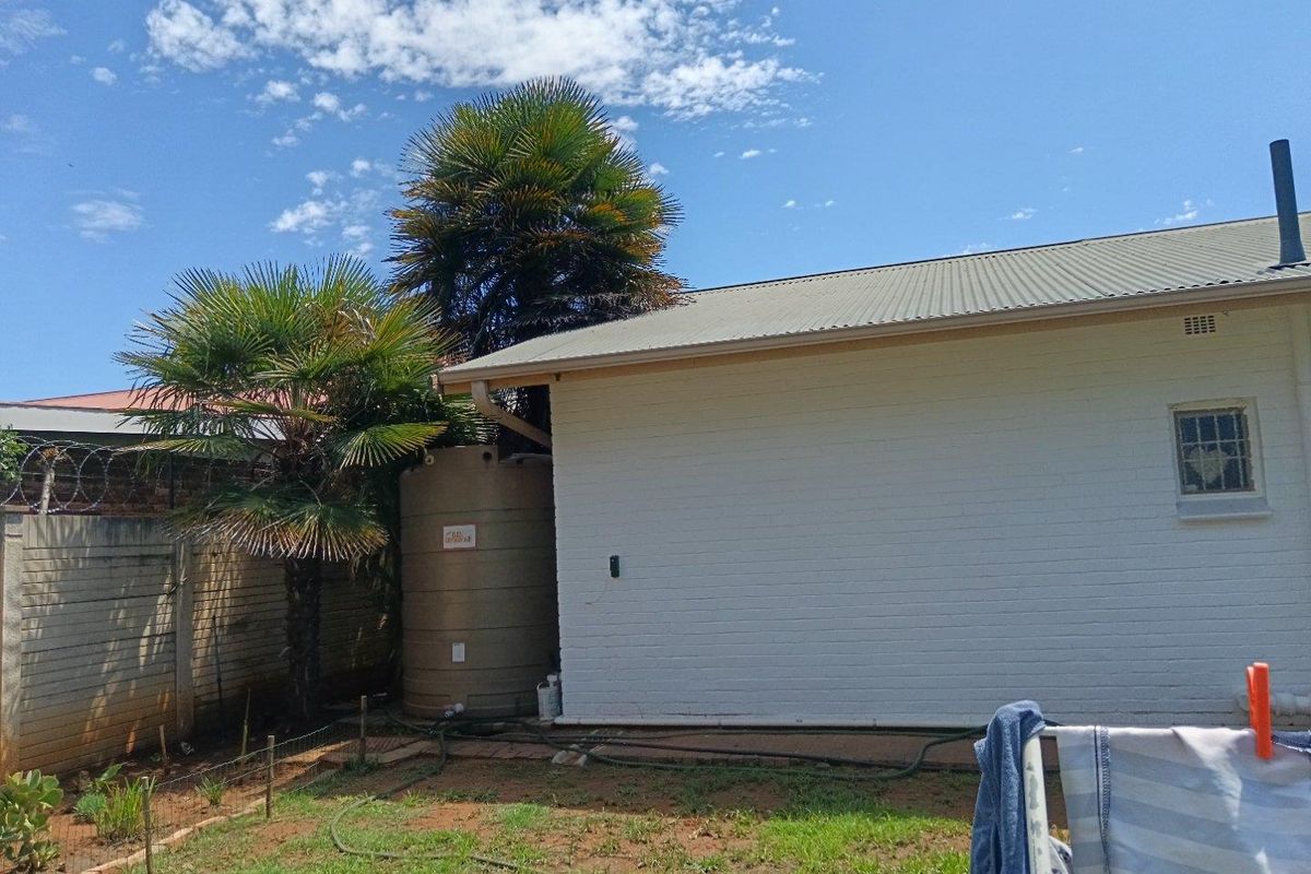 A view of the rear exterior of the house featuring a white brick facade, corrugated metal roof, and a large water storage tank.