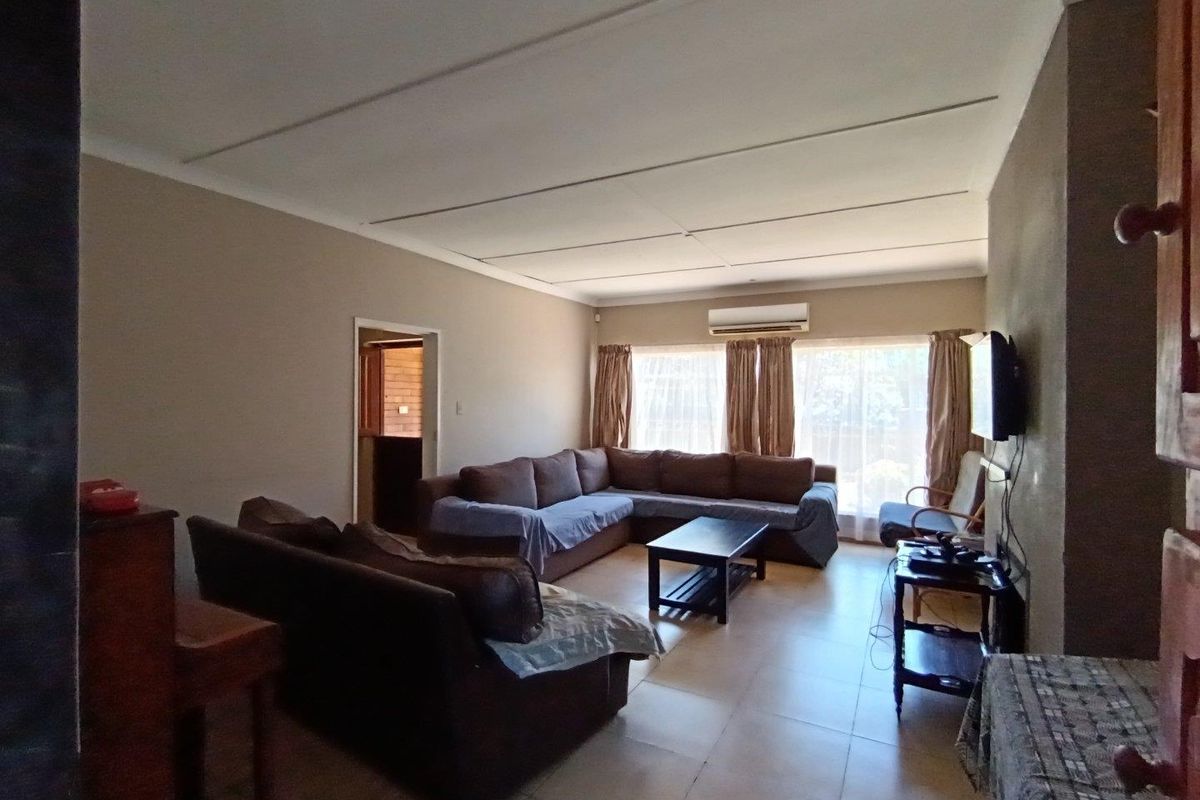 A spacious living room featuring tiled flooring, a wall-mounted air conditioning unit, and large windows allowing for natural light.