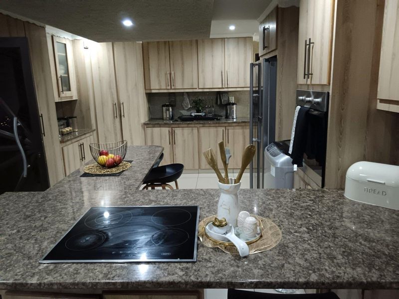 Modern kitchen featuring light wood-grain cabinetry, granite countertops, a central island with an integrated electric hob, and built-in oven.