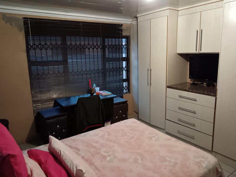 A bedroom featuring built-in cupboards, drawers, and tiled flooring, with venetian blinds and a security gate installed on the window.
