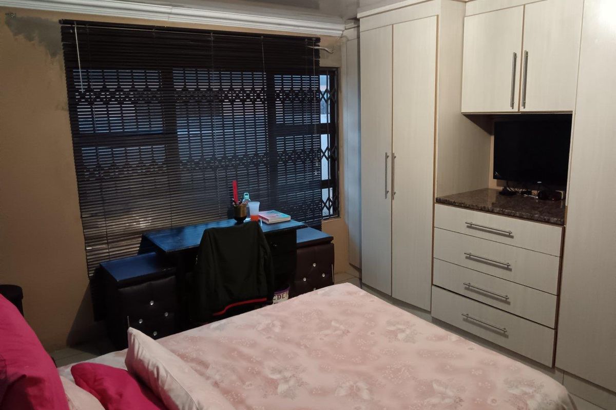 A bedroom featuring built-in cupboards, drawers, and tiled flooring, with venetian blinds and a security gate installed on the window.