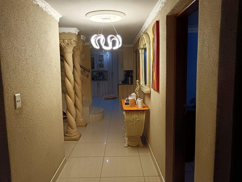 A well-lit hallway featuring decorative columns, tiled flooring, and ornate ceiling detailing, providing a transition space between the main living areas.