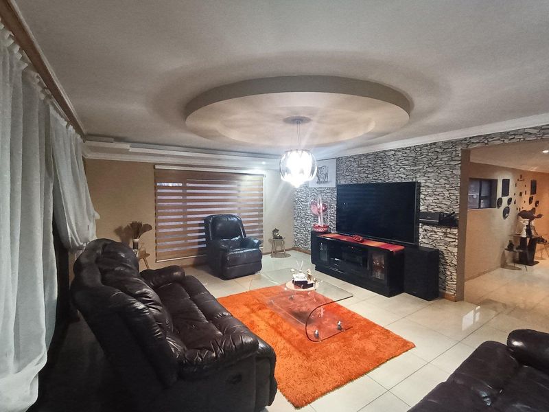 Spacious living room featuring a decorative circular recessed ceiling, stone-cladding accent wall, and neutral tiled flooring.
